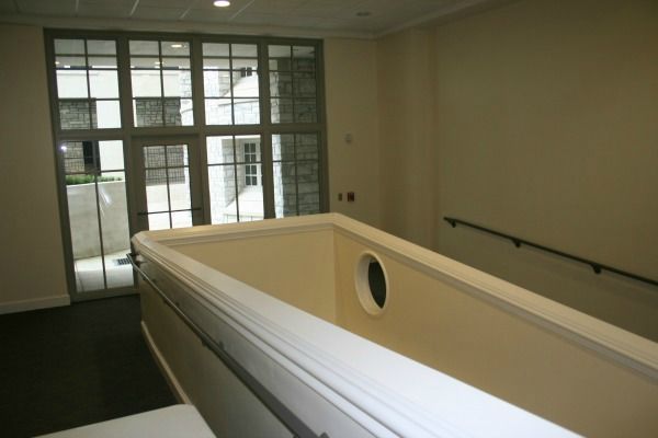 Interior view: white railing, doorway with grid windows, beige walls, and a staircase with a dark-colored floor.