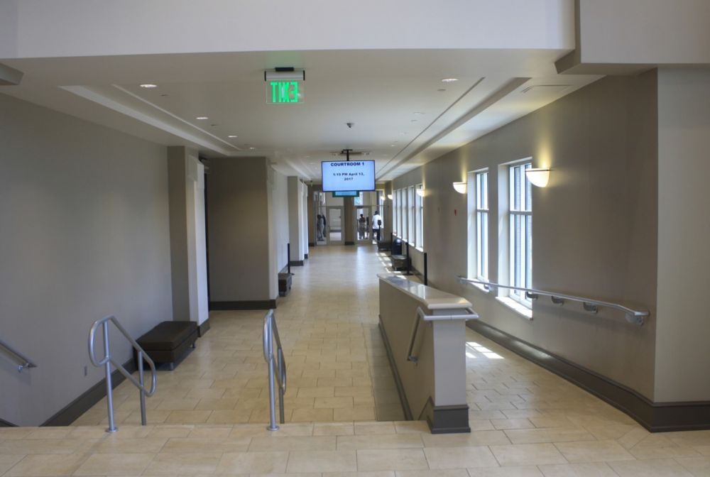 Hallway with stairs, beige tiles, windows, and a TV screen. Gray and white walls.