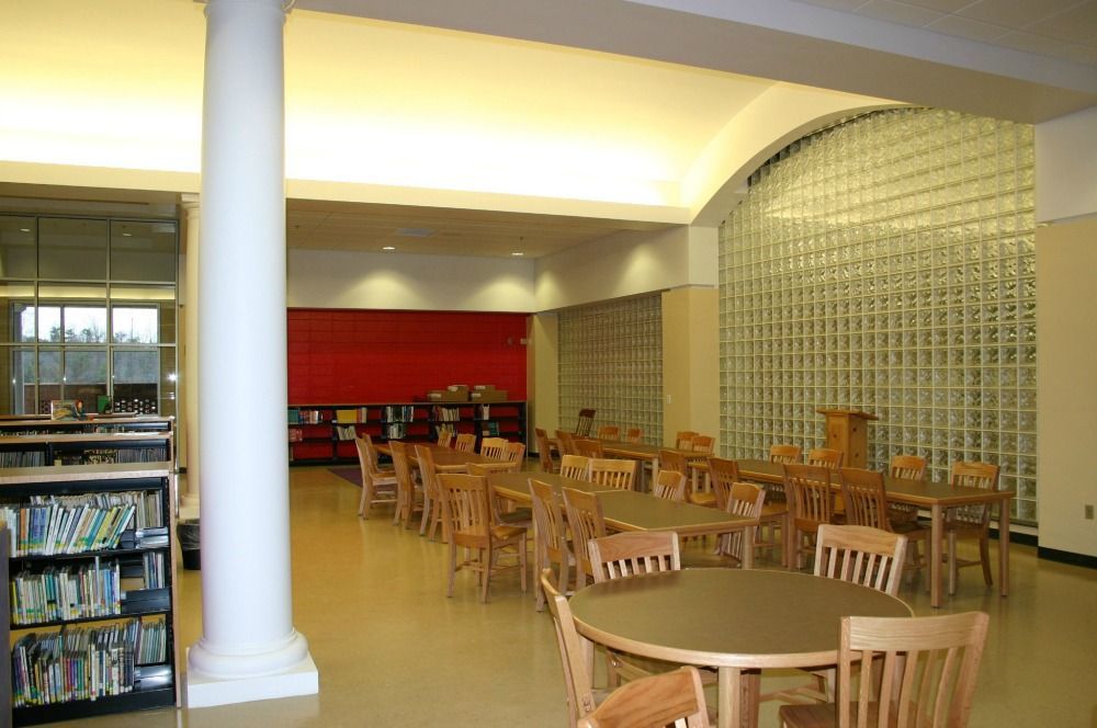 Library with tables and chairs, bookshelves, a red wall, and a glass block wall.
