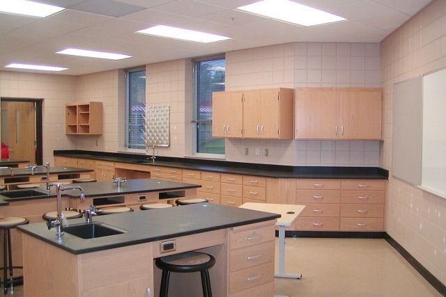 Science classroom with lab tables, cabinets, stools, and a whiteboard.