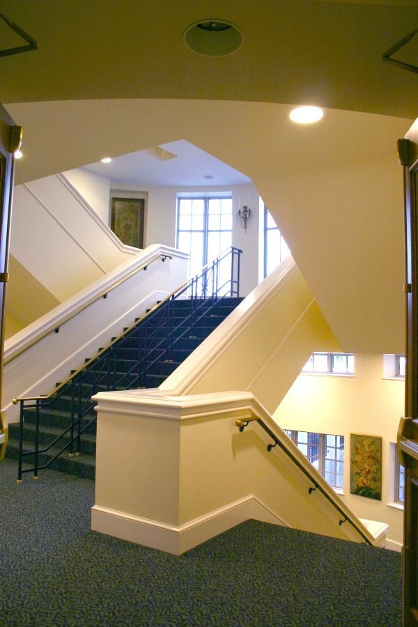 Staircase with black carpet, white walls, and handrails. Light enters from a window at the top.