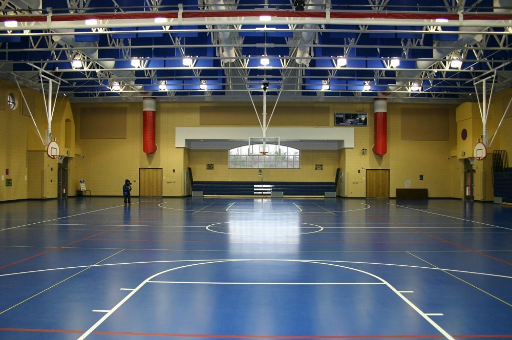 Blue basketball court in a gymnasium, with a basketball hoop and lights overhead.