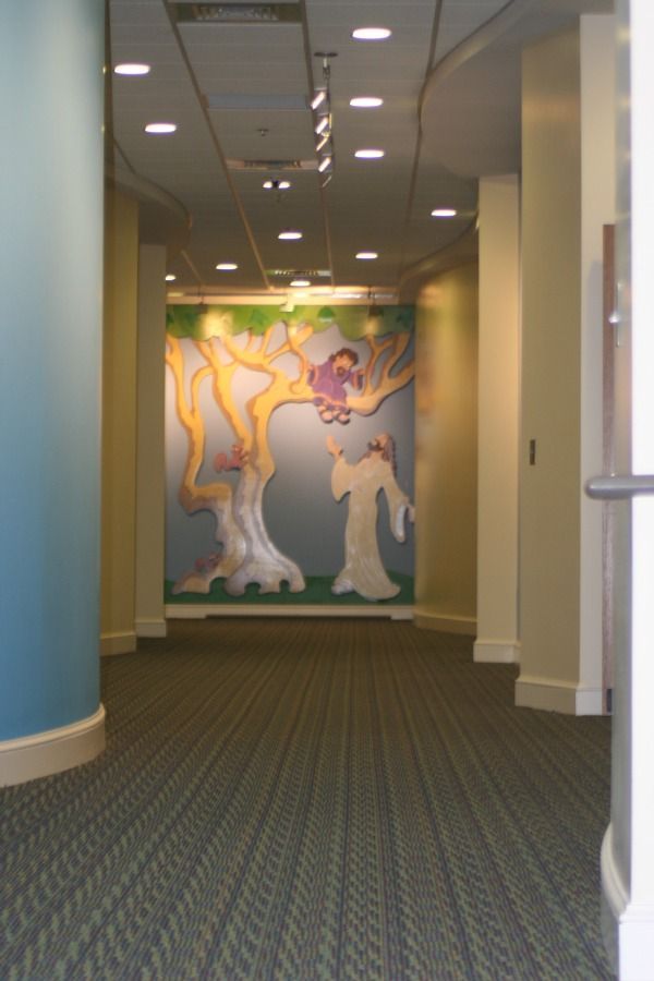 Hallway with a whimsical mural of a tree and figures; carpet, blue and beige walls.