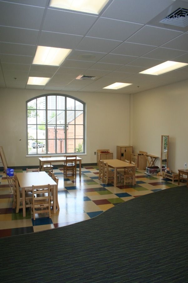Empty classroom with tables, a large window, and colorful tile floor.
