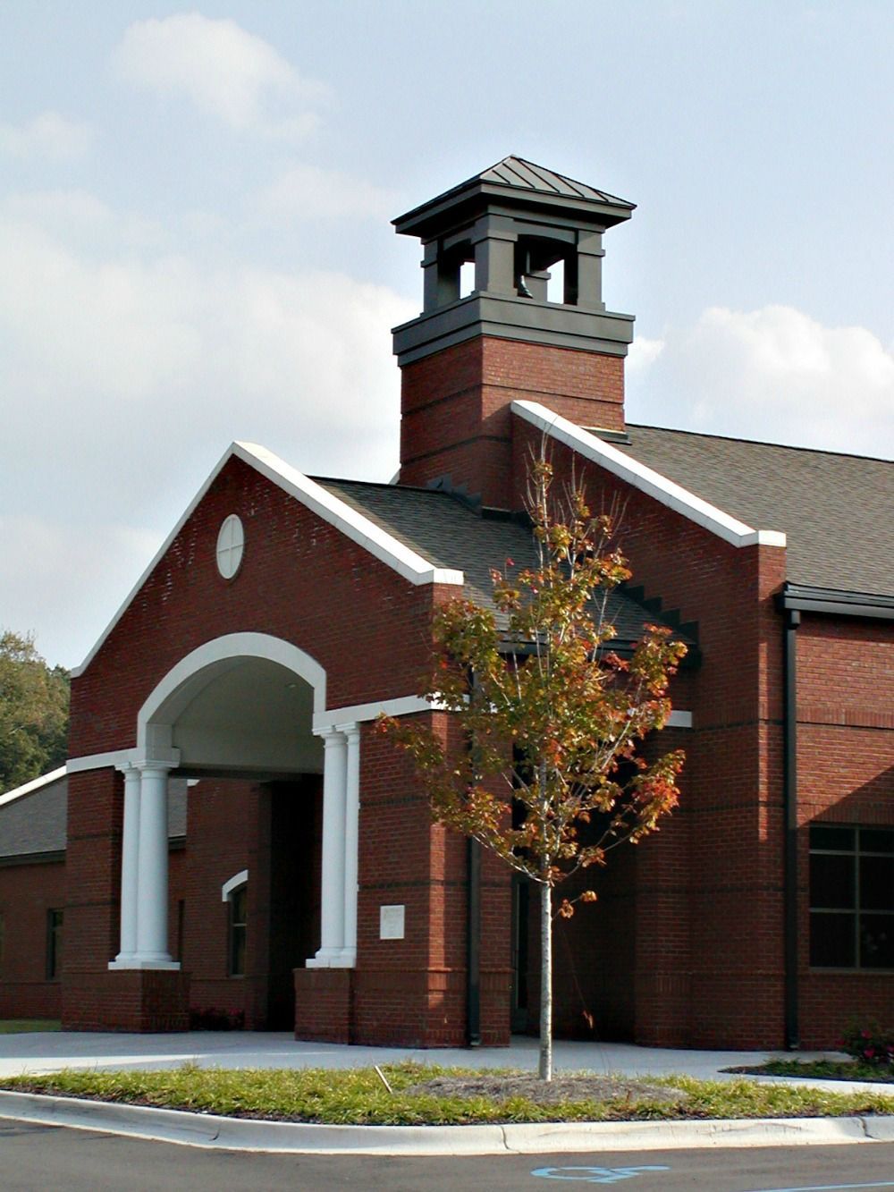 Red brick building with white accents; a bell tower, and a small tree in front.
