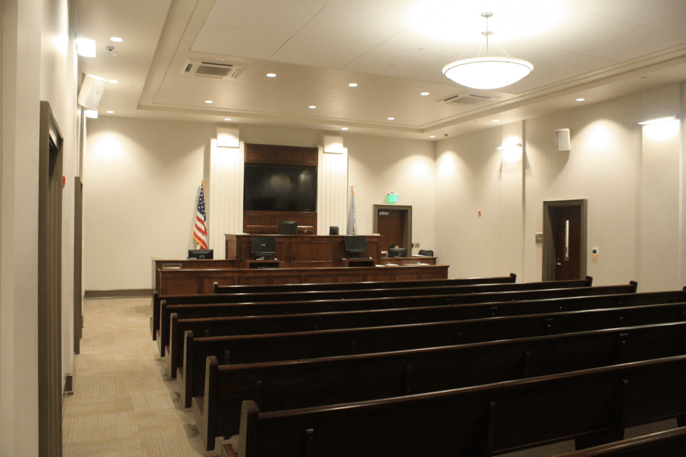 Empty courtroom with rows of wooden pews facing a judge's bench and the American flag.
