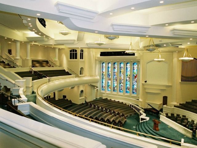 Interior of a large church auditorium with multiple levels of seating, stained glass window, and organ.