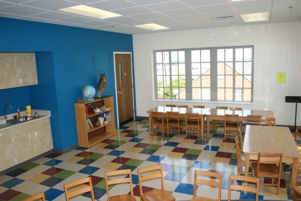 Classroom with blue wall, colorful checkered floor, tables, chairs, and a window.