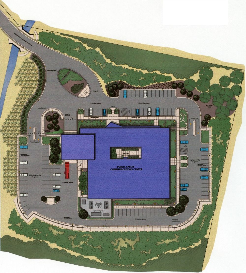 Top-down view of a building with blue roof, parking lot, landscaping and surrounding foliage.