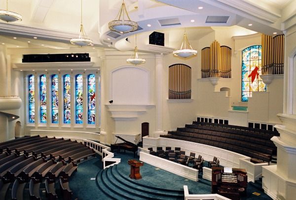 Interior of a church with rows of seating facing a pulpit, organ pipes, and stained-glass windows.