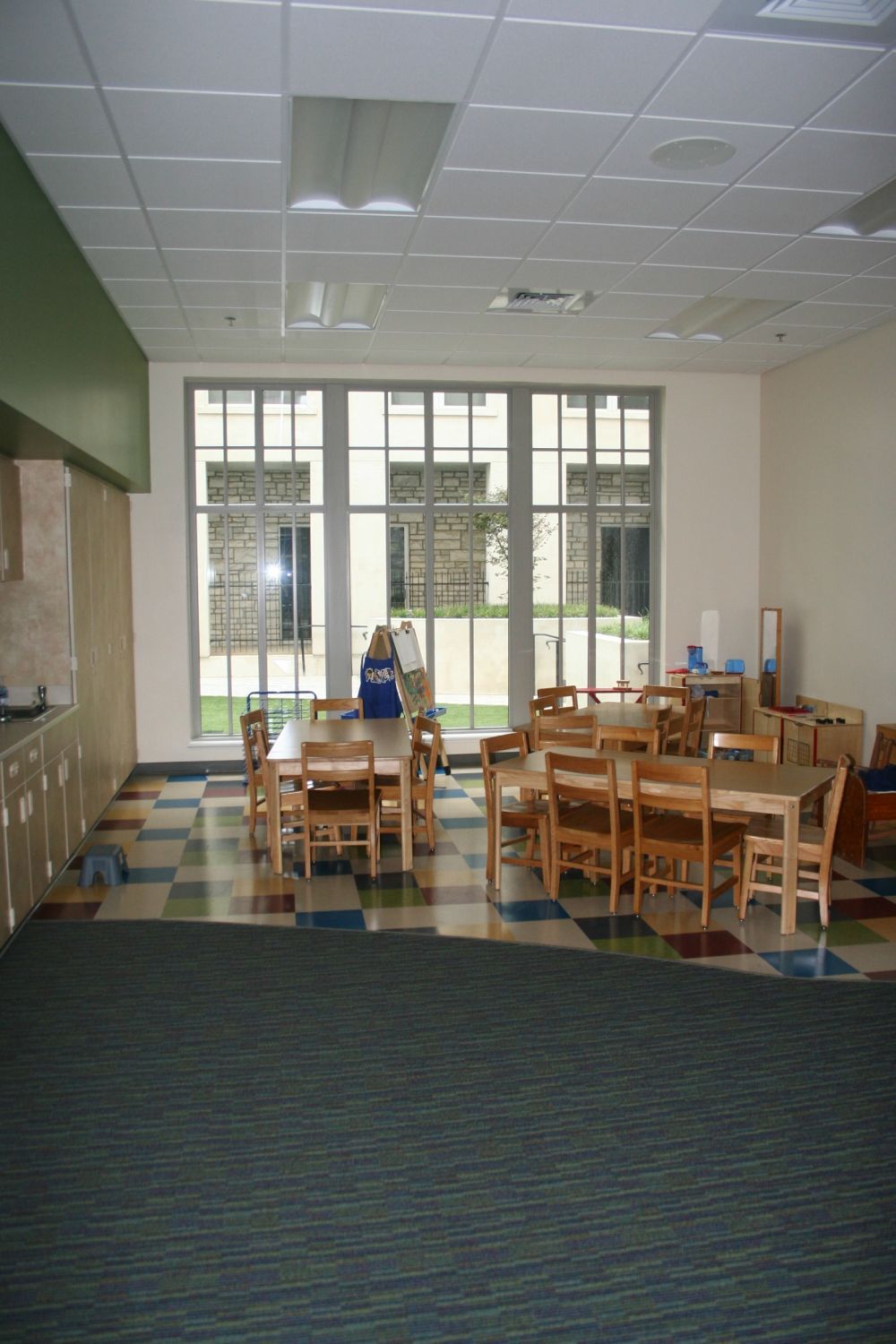 Dining room with tables and chairs, checkered floor, large window, and green wall.