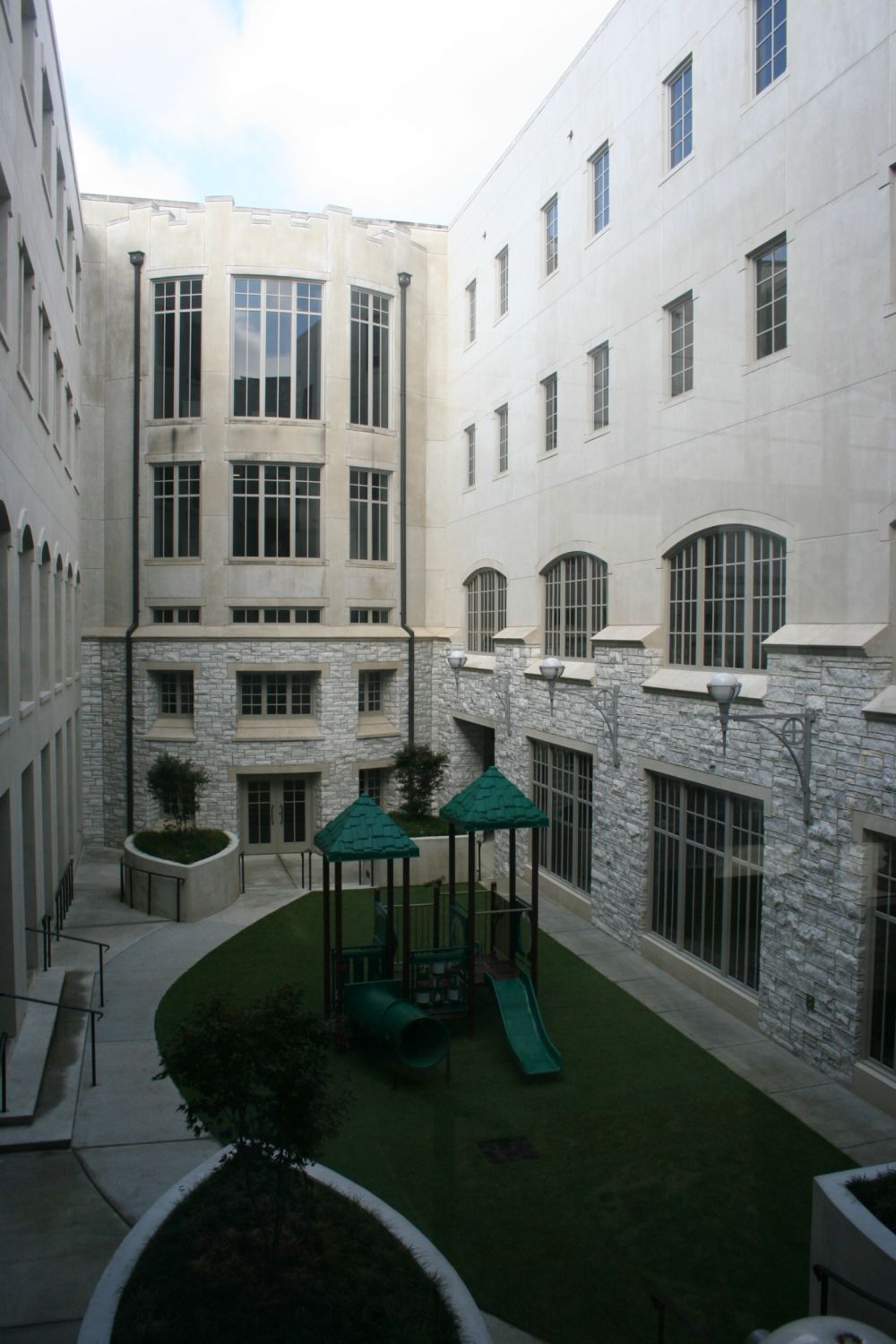 Courtyard with playground, surrounded by light-colored stone buildings with many windows.
