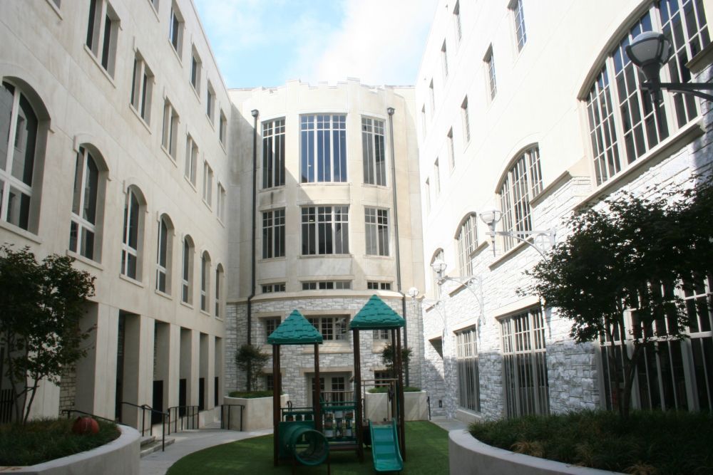 Courtyard with a small playground surrounded by a multi-story building with arched windows.