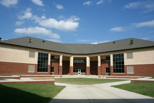 School building with red brick, tan walls, and large windows under a blue sky with clouds.
