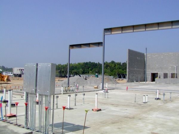 Construction site with exposed rebar, concrete foundations, steel beams, and a partially built cinder block wall.