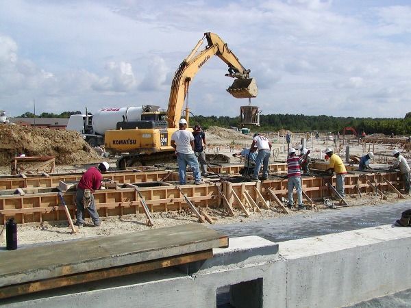 Construction site with workers setting forms, an excavator loading material.