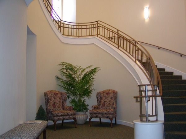 A staircase with a curved railing, two patterned chairs, and a potted plant in a light-colored entry hall.