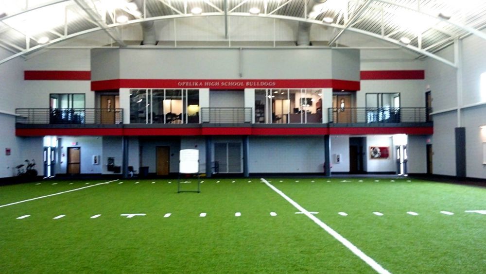 Indoor sports facility with green turf field, red accents, and two-story structure.