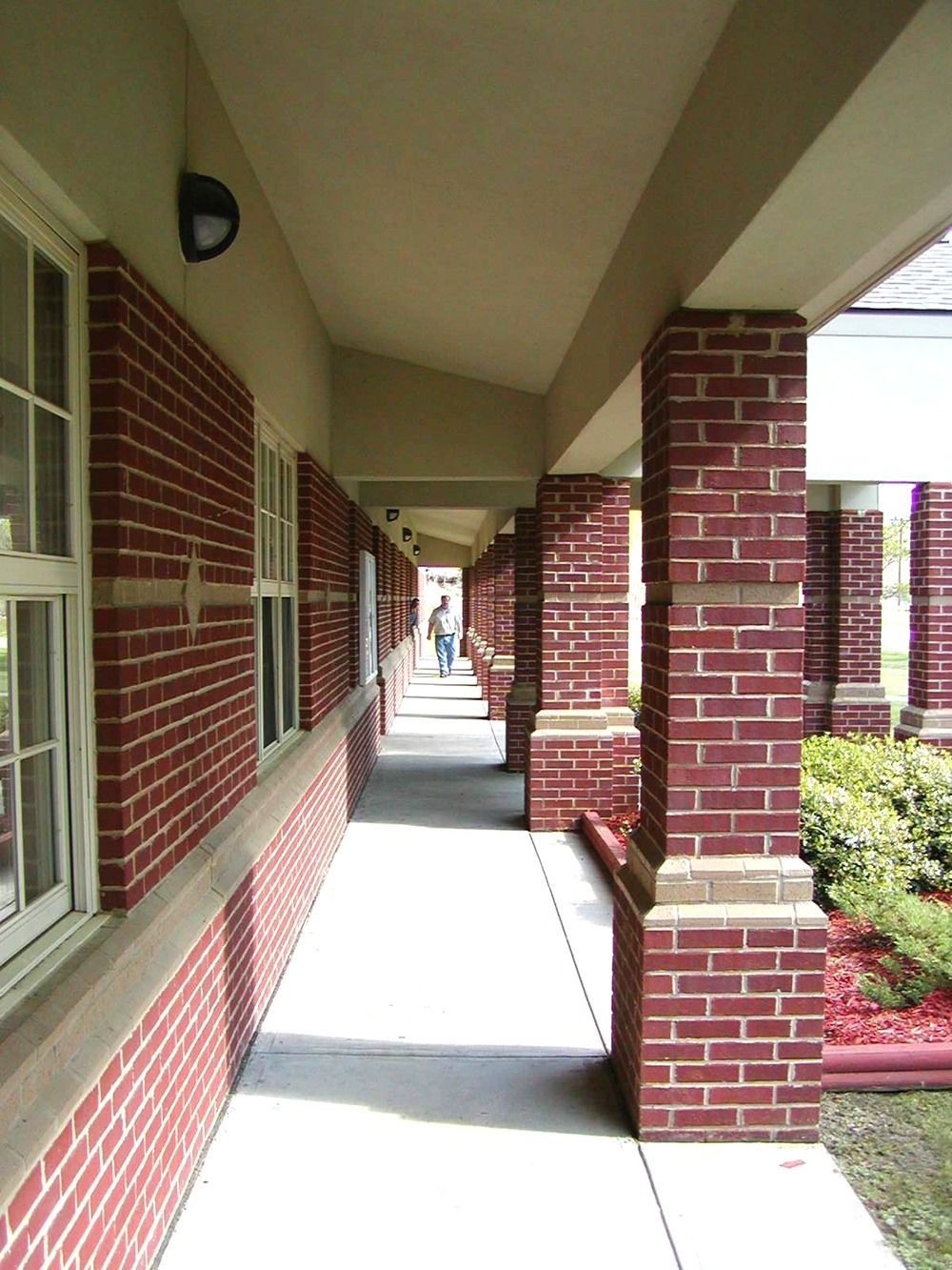 Covered brick walkway, red brick columns, white windows, person walking in the distance.