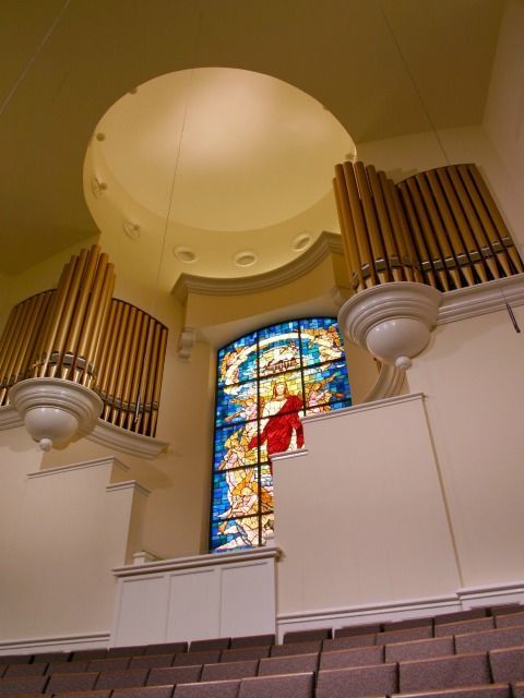 Church interior with stained-glass window, organ pipes, and domed ceiling.