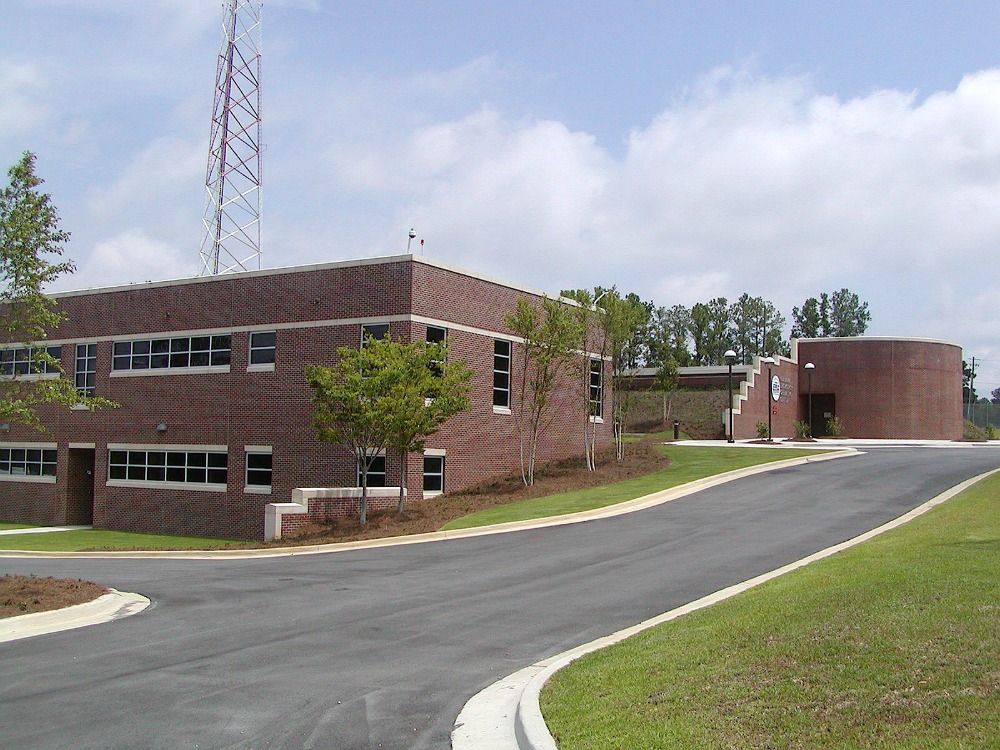 Brick building with a radio tower, asphalt road, and grassy lawn on a partly cloudy day.