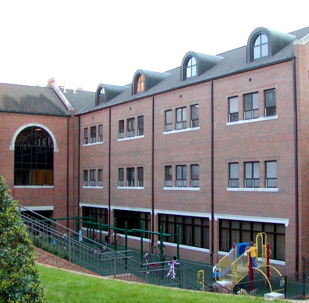Brick building with arched windows, dormers, playground, and children playing on a sunny day.