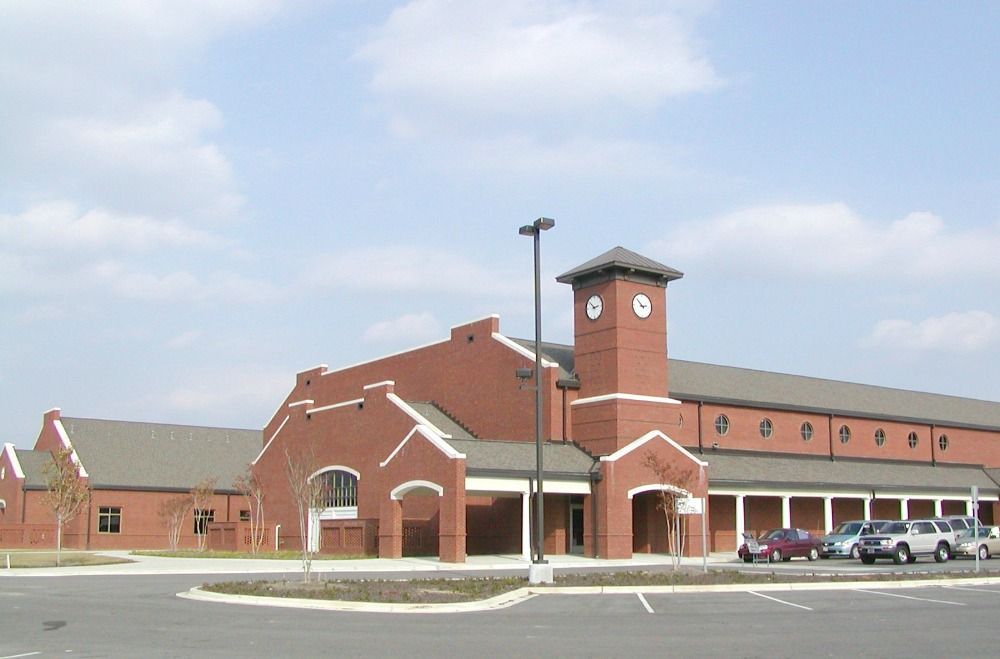 Red brick building with clock tower; parking lot with cars.