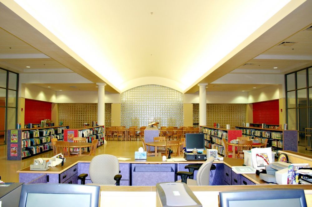 Library interior: check-out desk, bookshelves, tables, chairs, and a frosted glass wall.