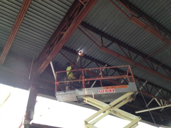 Welder on a lift working on the metal structure of a building's ceiling.