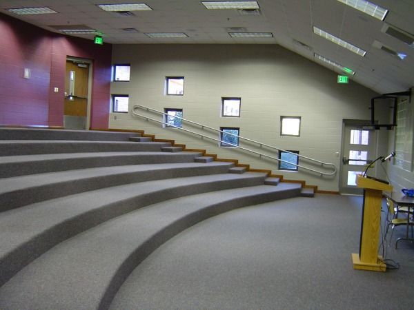 An empty auditorium with tiered seating and small square windows along the wall.