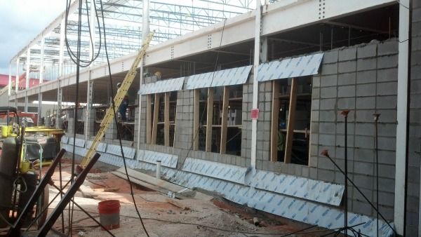 Construction site with a partially built building. Exterior walls of concrete blocks, wood window frames, and metallic sheathing.