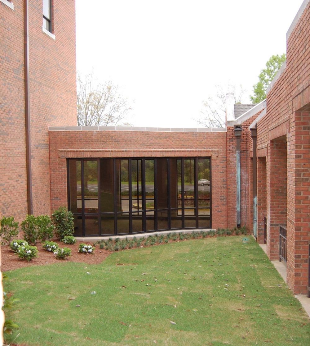 Brick building exterior with large window and small grassy area.