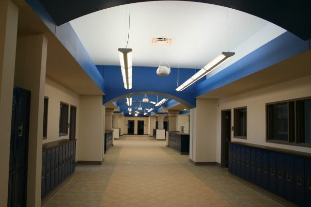 School hallway with blue lockers and arched ceiling; fluorescent lights illuminate the space.