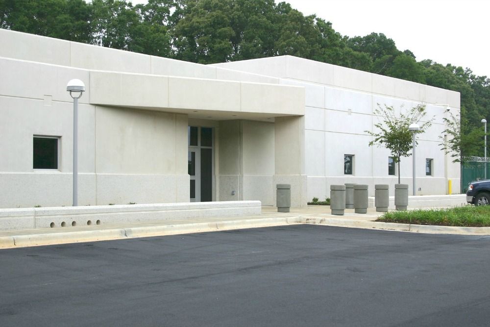 Exterior of a modern, beige building with a recessed entrance, trees, and a dark asphalt parking lot.