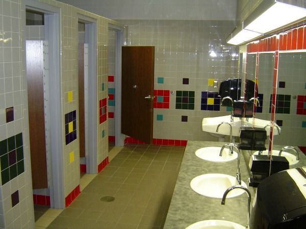 Public restroom with white tiled walls, colorful accents, and sinks.
