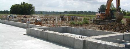 Construction site with concrete foundations being built; excavator in the background.