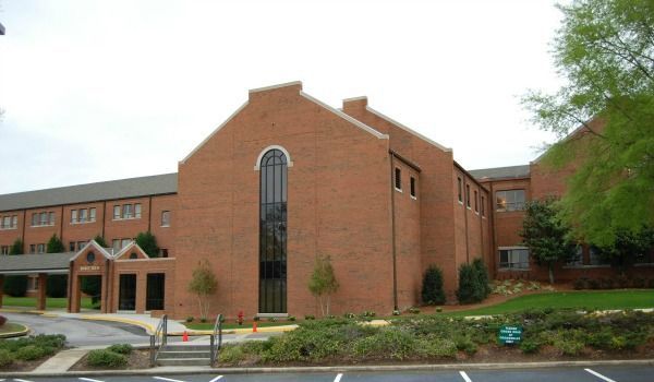 Brick building with tall arched window, entrance canopy, and green landscaping.