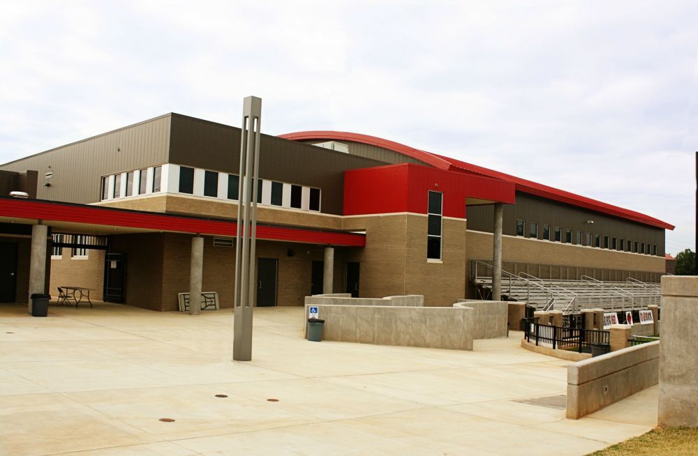 Modern school building with a red and brown facade, concrete courtyard.
