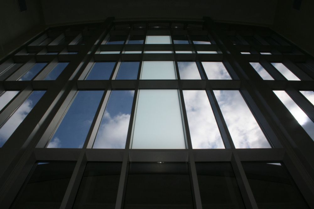 Looking up at a large glass window grid showing cloudy blue sky and a light-colored rectangle.