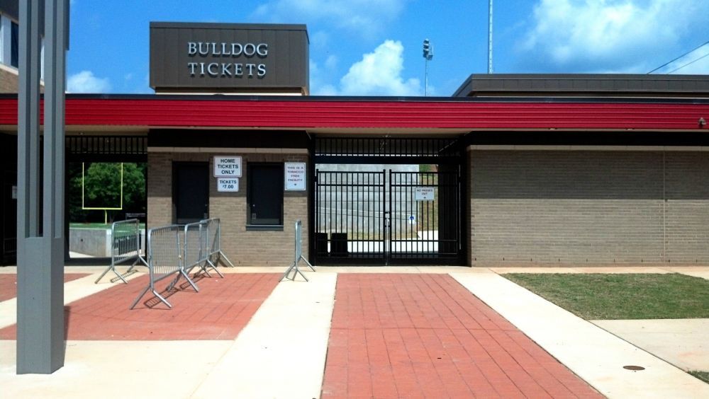 Bulldog Tickets booth at a stadium entrance with red and gray accents, a brick walkway, and metal barriers.