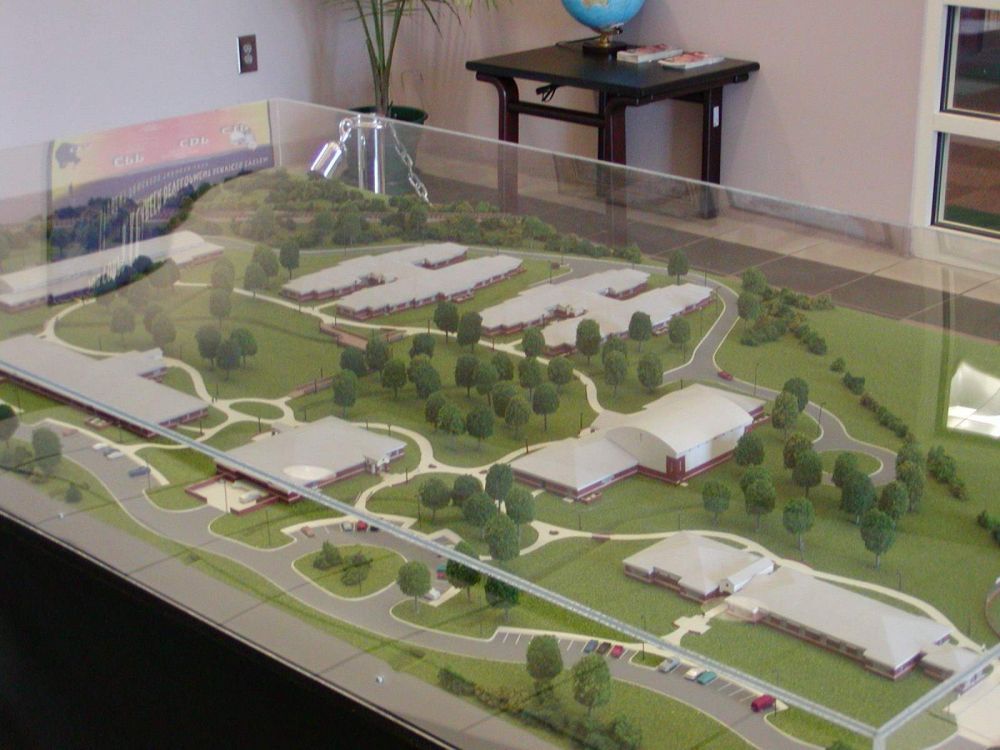 Architectural model of a complex with buildings, roads, trees, and surrounding landscape.