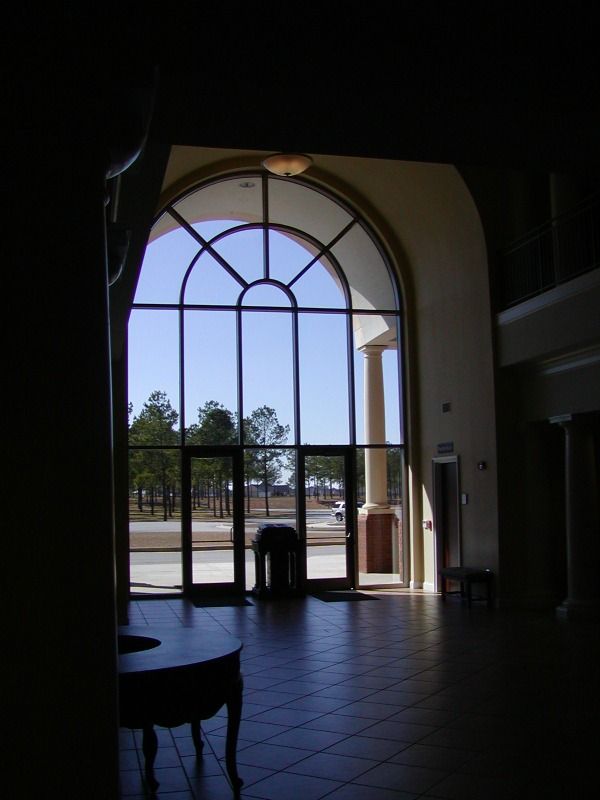 Interior view of a building with arched window looking out to trees and a blue sky.
