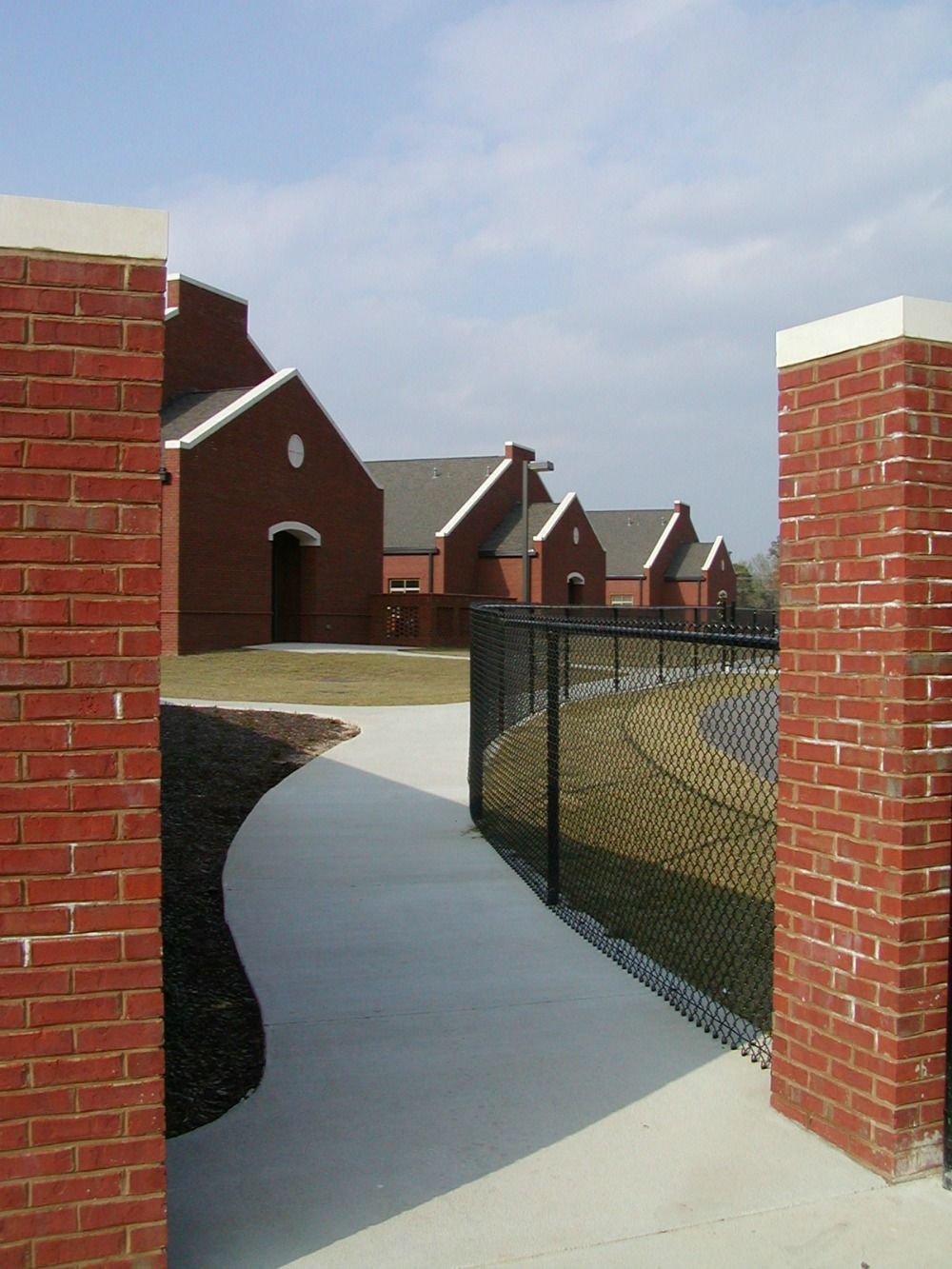 Brick entranceway leads to red brick buildings with light blue sky.