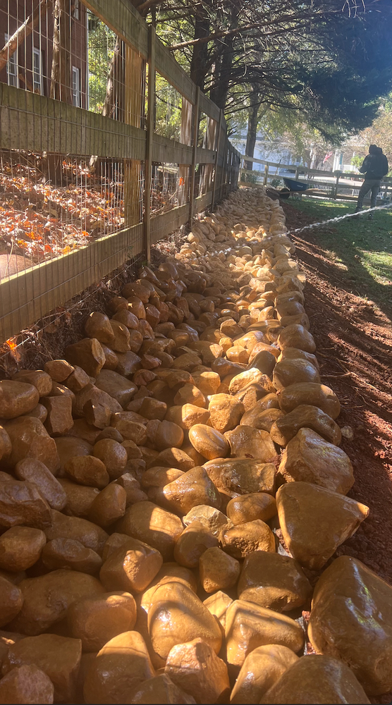 RC Landscapes constructing a stone retaining wall on a sunny day.