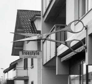 Eine Schere, die an der Seite eines Gebäudes hängt, mit einem Schild mit der Aufschrift „Freestyle Coiffure“