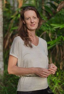 Practitioner Rebecca Rose  standing peacefully outdoors standing in front of lush tropical plants