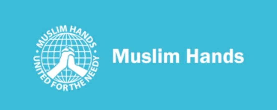 Logo for Muslim Hands, a charity. Features a blue background with the organization's name and a white emblem of clasped hands in front of a globe.