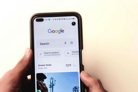 A person is holding a cell phone with the google search page open.