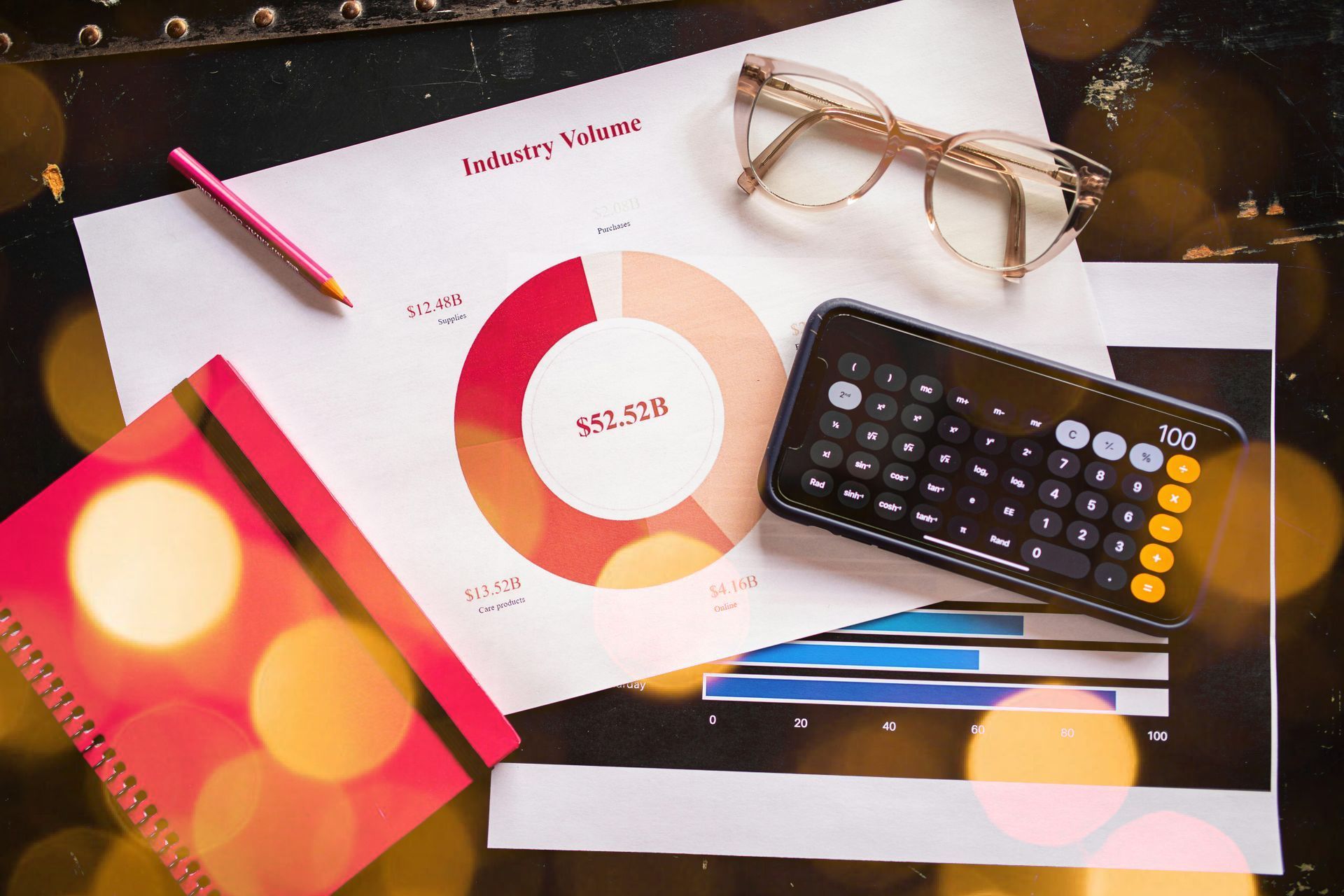 A phone , calculator , glasses , and a notebook are on a table.