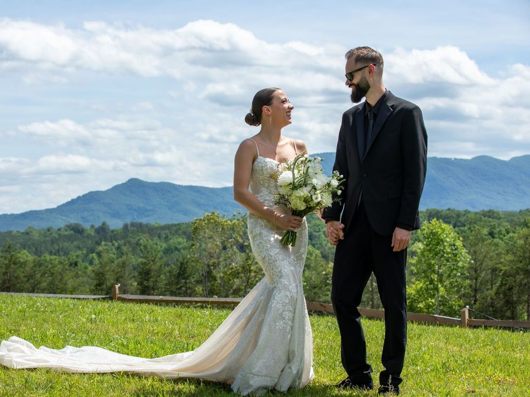 Bride with flowing gown and groom gazing lovingly at mountaintop ceremony spot at Serenity Ridge wedding venue.
